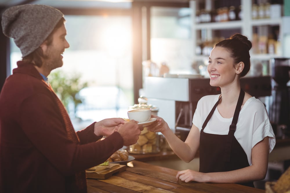 Waitress serving a cup of coffee to customer in cafe